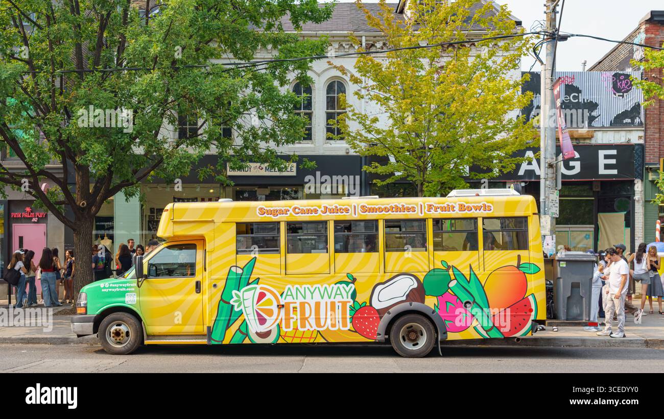 Un food truck jaune vif décoré de motifs de fruits propose du jus de canne à sucre, des smoothies et des bols de fruits dans une rue animée. Banque D'Images