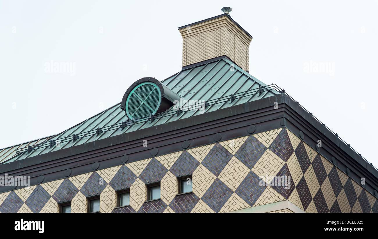 Une façade à motifs avec des tuiles en forme de losange soutient un toit en métal vert surmonté d'un évent circulaire et d'une cheminée en brique. Banque D'Images