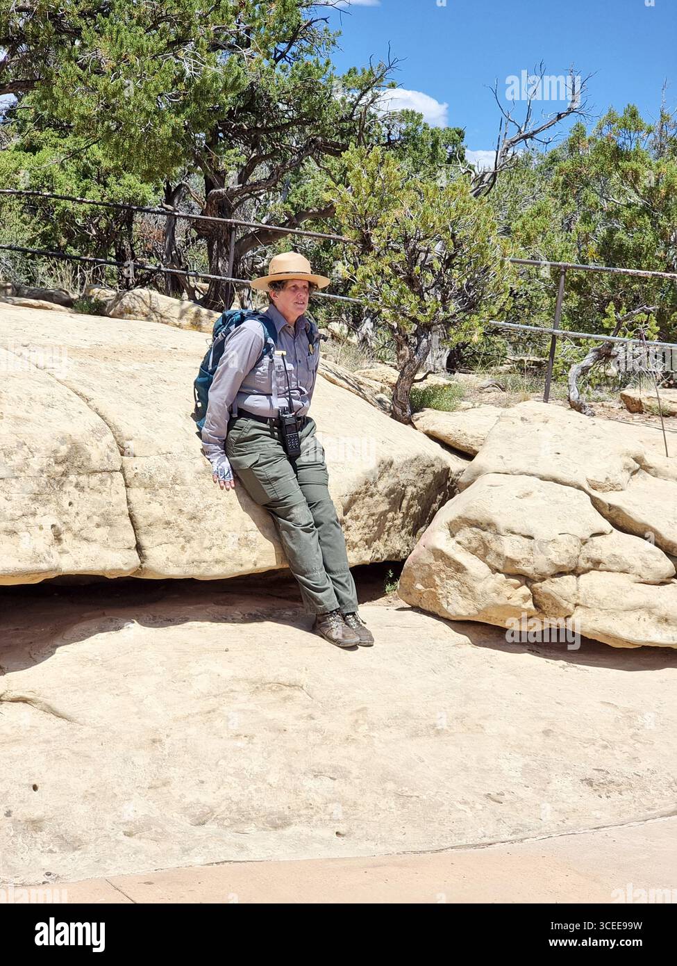 Gardien de parc féminin dans une tenue de gardien typique appuyée contre un gros rocher jaune dans le parc national de Mesa Verde, Colorado, États-Unis - Image de stock capturée avec un smartphone Gardien de parc féminin dans une tenue de gardien typique appuyée contre un gros rocher jaune dans le parc national de Mesa Verde, Colorado, États-Unis - Image de stock capturée avec un smartphone