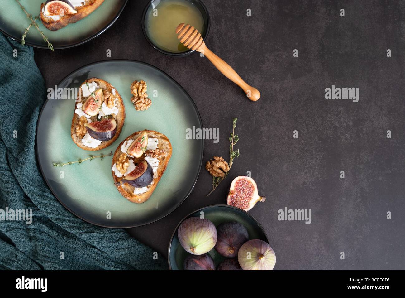 Vue de dessus horizontale de toasts de fromage de chèvre figues sur une assiette verte avec une trempette de miel et une serviette sur fond noir Banque D'Images