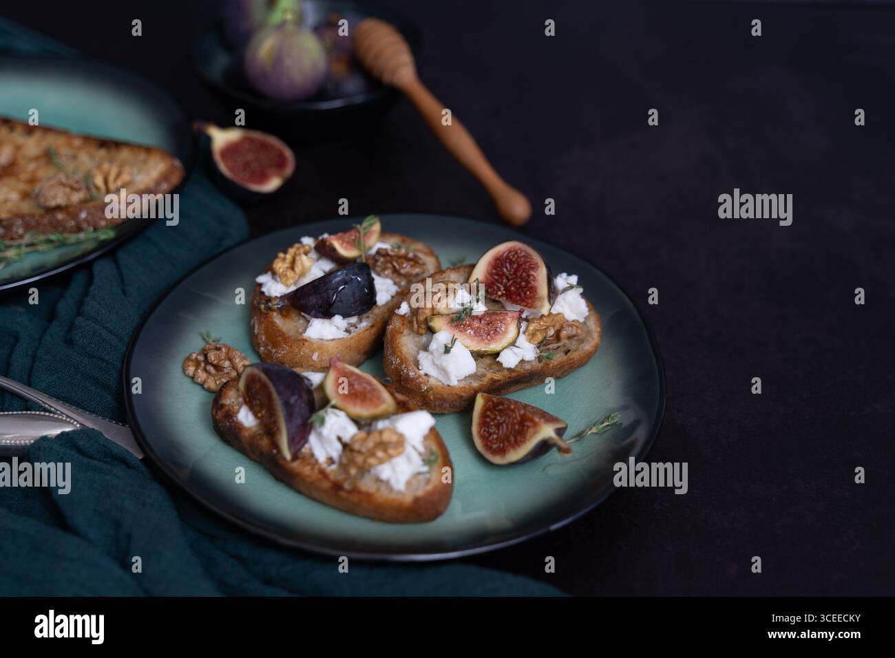 Vue de face horizontale de trois toasts au fromage de figues et de chèvre sur une assiette verte avec trempette au miel, noix, thym, serviette de cuisine verte, espace copie Banque D'Images