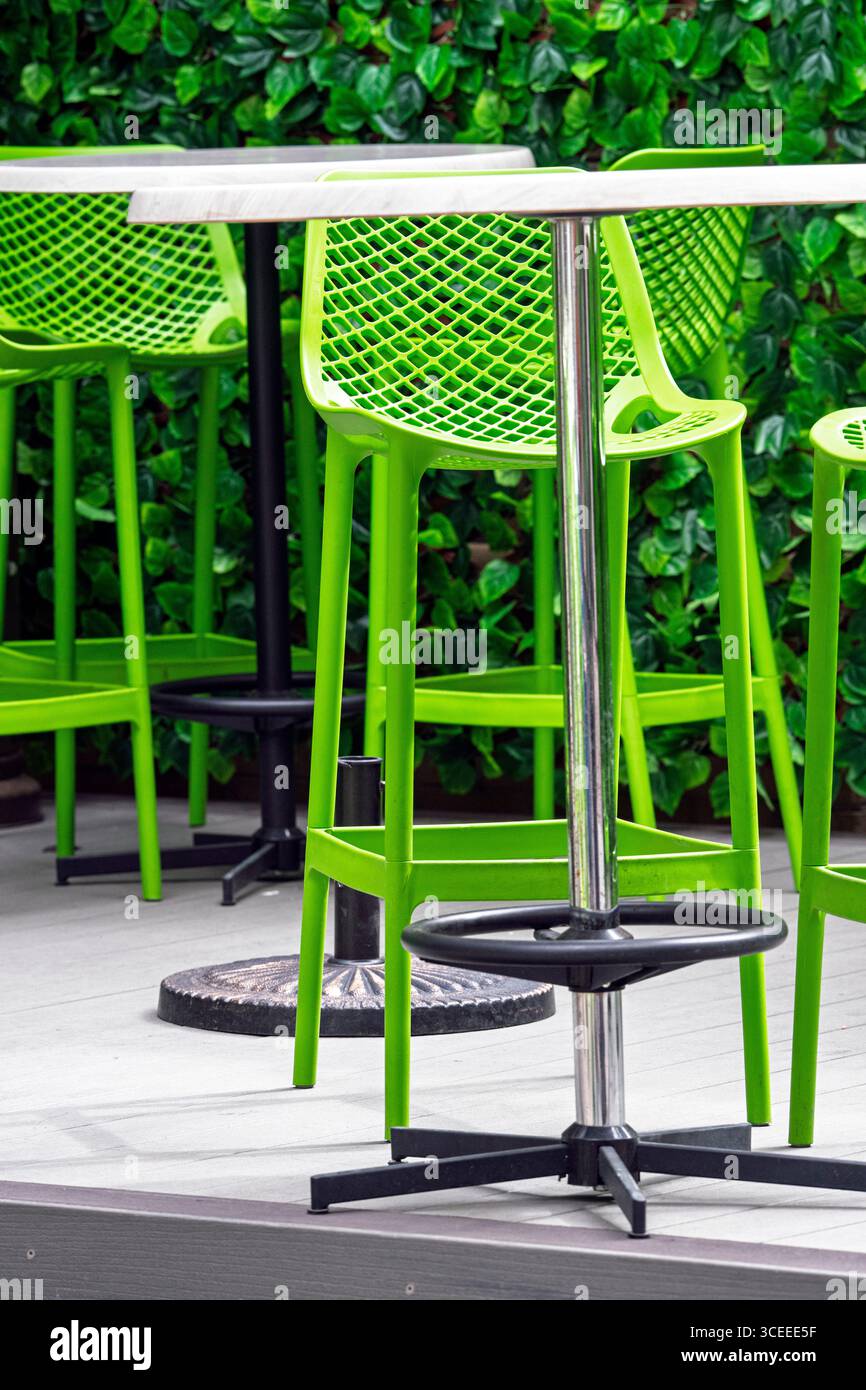 Café moderne en plein air avec tabourets de bar et tables verdoyants sur fond de mur verdoyant, créant une atmosphère fraîche Banque D'Images