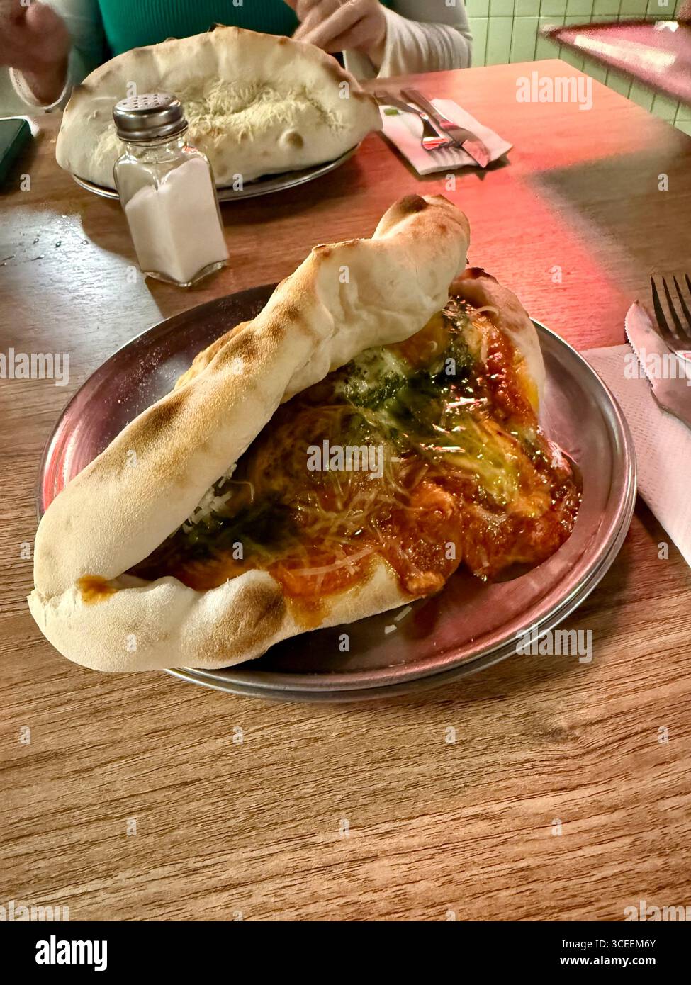 Un sandwich copieux avec du fromage fondu, de la viande grillée et des légumes frais servis sur une planche de bois, capturé dans un environnement de restaurant confortable. - Image de stock capturée avec un smartphone