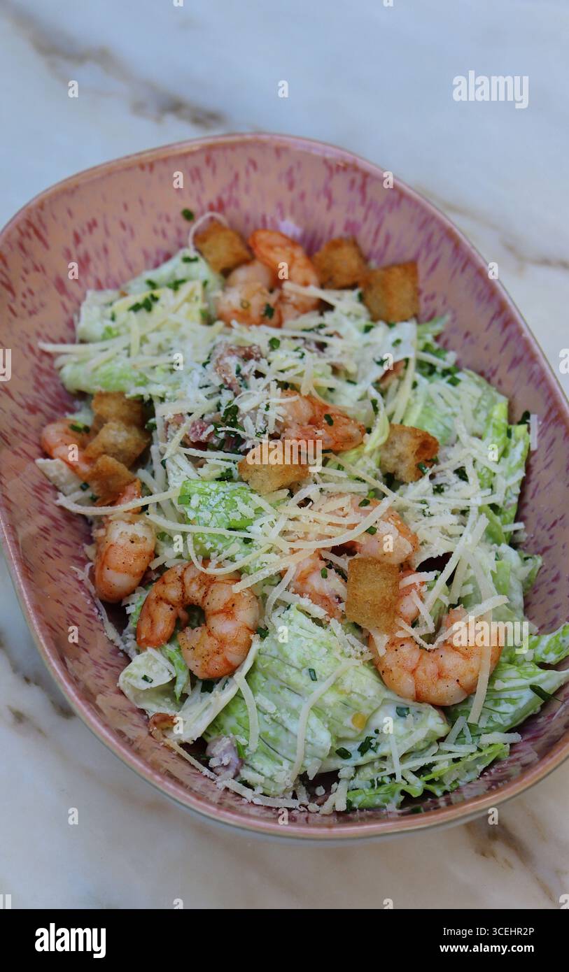 Salade César fraîche servie dans un bol en céramique rose avec crevettes grillées, laitue romaine croquante, parmesan, croûtons croustillants et vinaigrette crémeuse. Banque D'Images