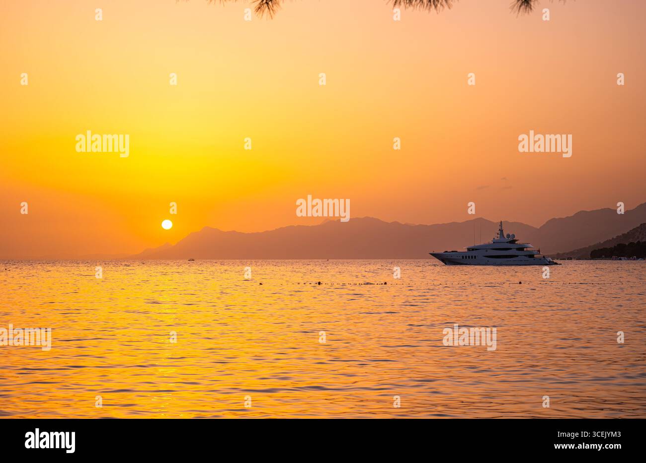 Yacht de luxe sur la mer Adriatique au coucher du soleil près de Makarska Croatie avec silhouette de montagne Biokovo et reflets de ciel orange doré Banque D'Images
