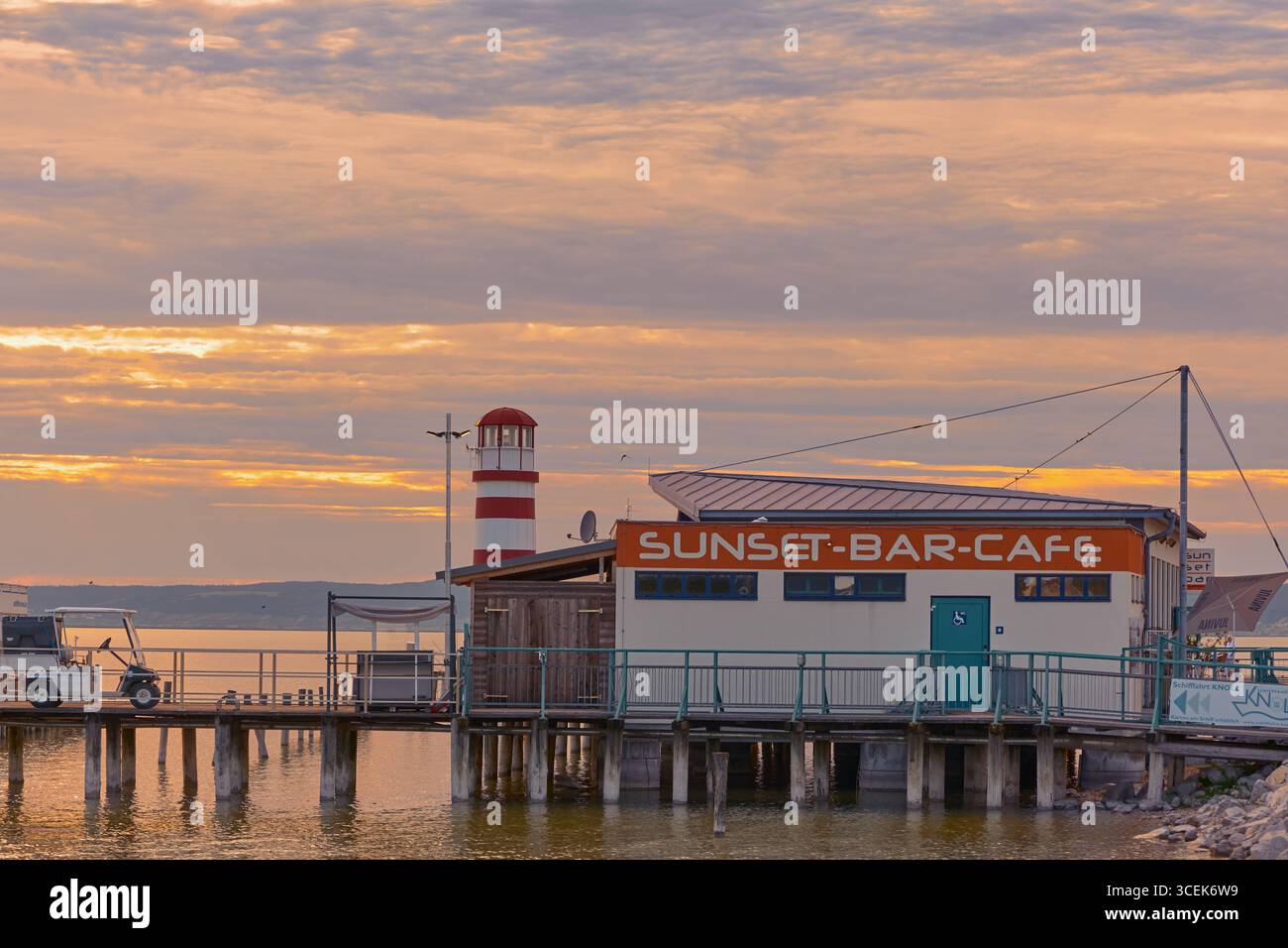 Bar au coucher du soleil au bord du lac sur un quai avec une vue panoramique sur le phare de Podersdorf au lac Neusiedl, Autriche, pendant la lumière dorée du soir. Banque D'Images