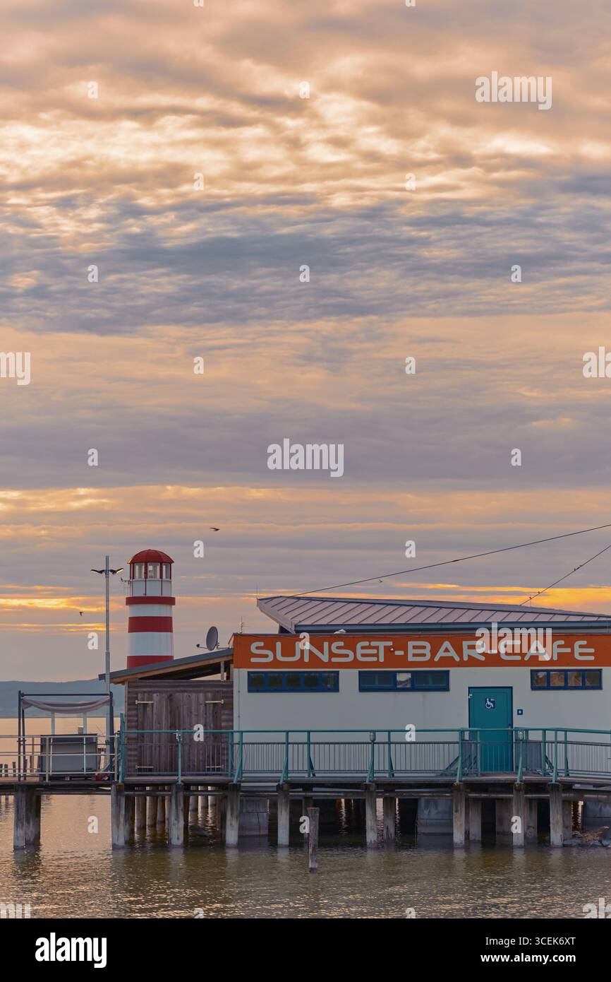 Charmant café sur une jetée au bord du lac Neusiedl, Autriche, offrant une vue imprenable sur le phare de Podersdorf au-dessus des eaux calmes. Banque D'Images