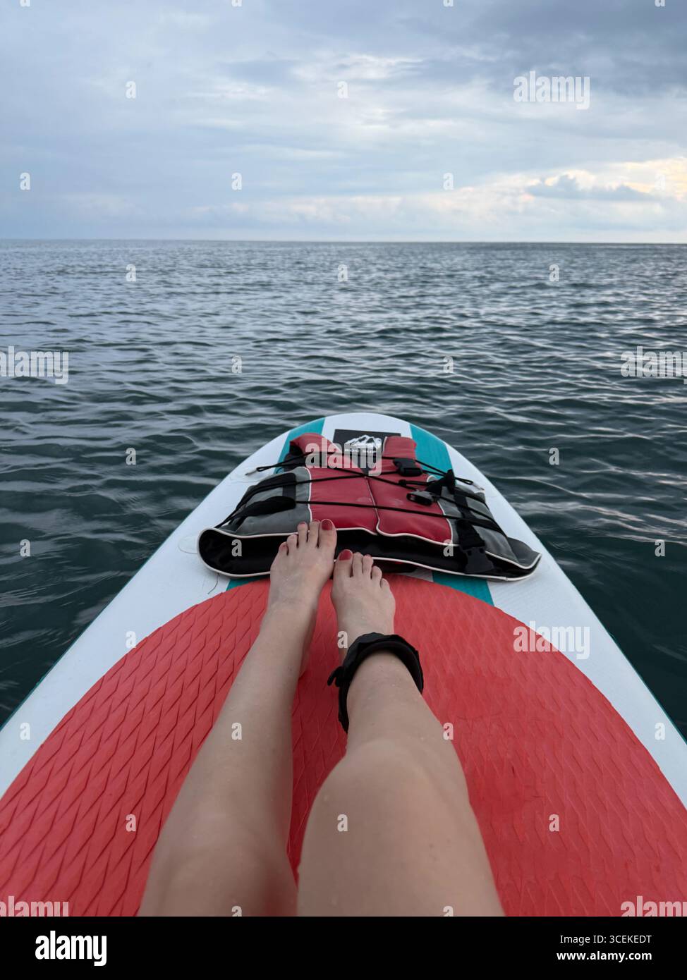 Cette photo montre une personne allongée ou assise sur un stand-up paddleboard (SUP) en pleine mer. Leurs pieds et leurs jambes sont visibles, avec un attac de laisse de cheville Banque D'Images