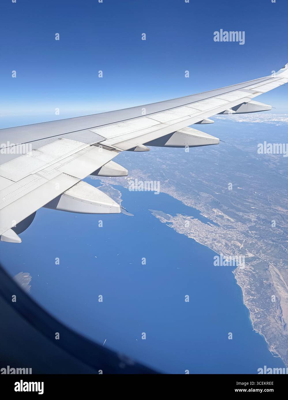 La vue aérienne depuis la fenêtre de l'avion capture l'aile contre un ciel dégagé et une vue côtière en dessous. Mer bleu profond rencontre un littoral créant une belle Banque D'Images