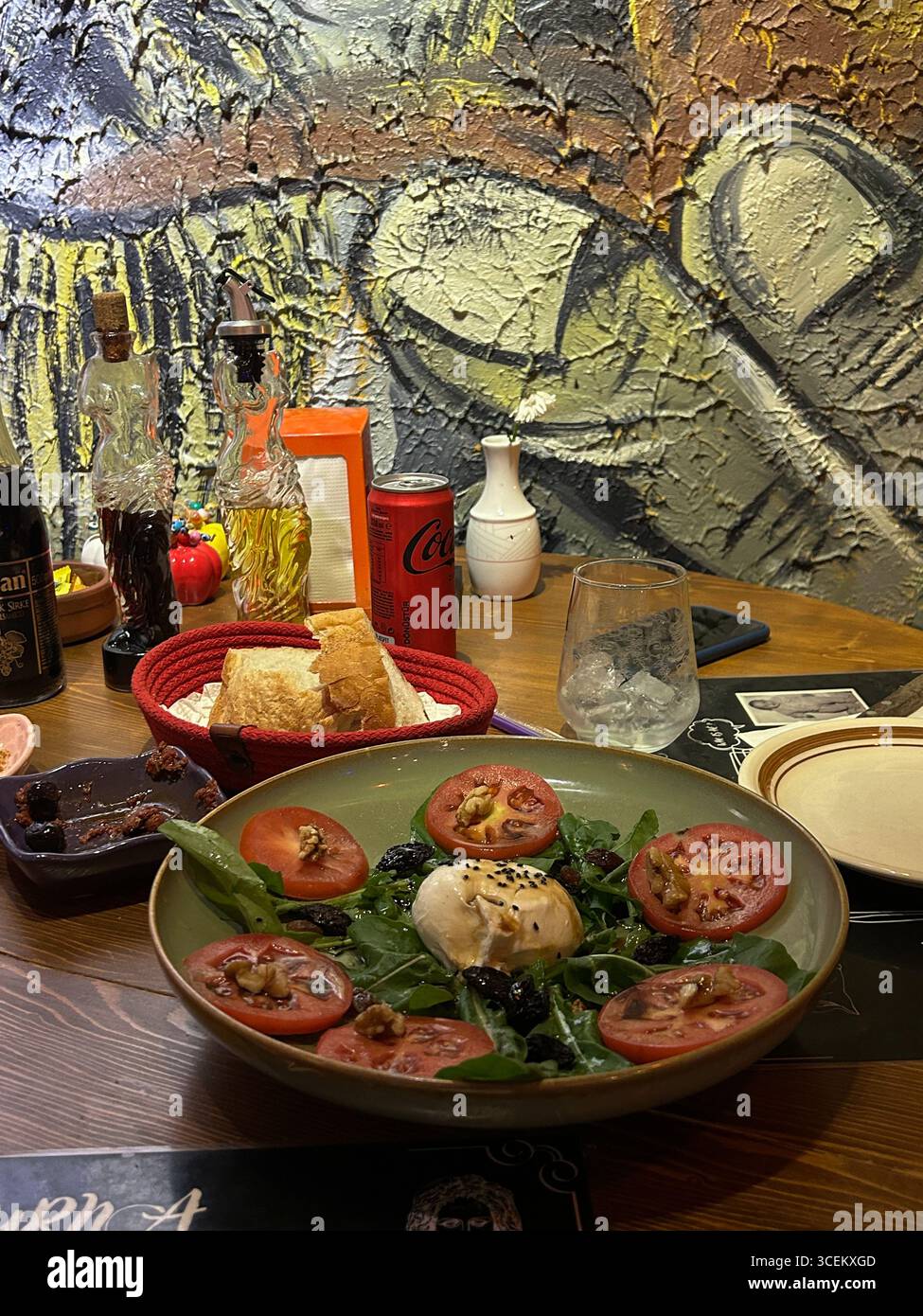 Cette image montre une salade de burrata fraîche avec des tranches de tomates, des noix, des olives et des légumes verts à feuilles. Pain dans un panier rouge, huile d'olive, vinaigre, Banque D'Images