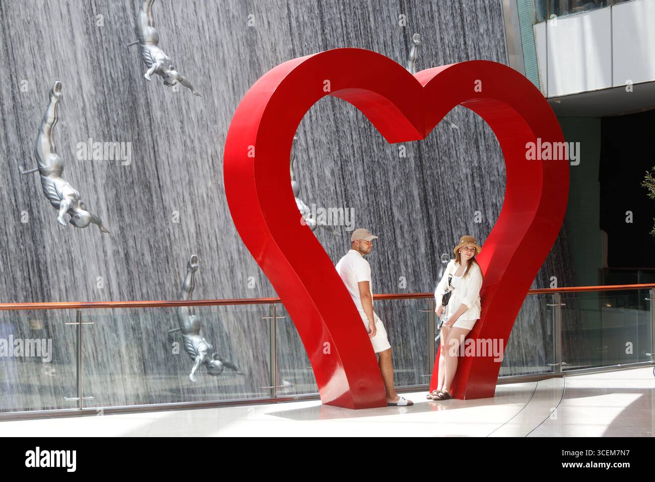 Couple posant devant une grande sculpture de coeur rouge près d'une cascade avec des statues de plongeurs au centre commercial dubai Mall UAE Banque D'Images
