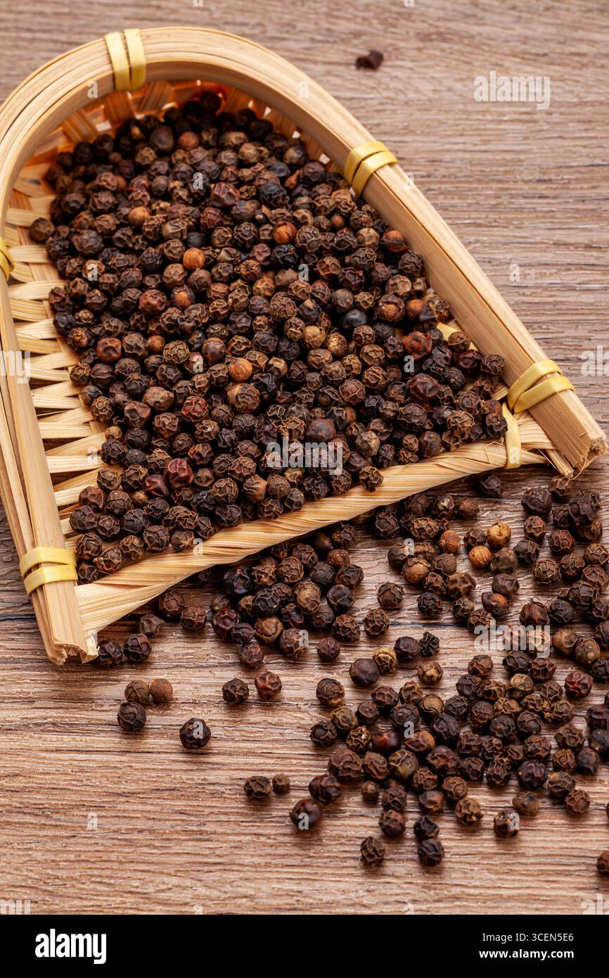 Grains de poivre noir renversant du panier de vinification traditionnel en bambou sur bois Banque D'Images