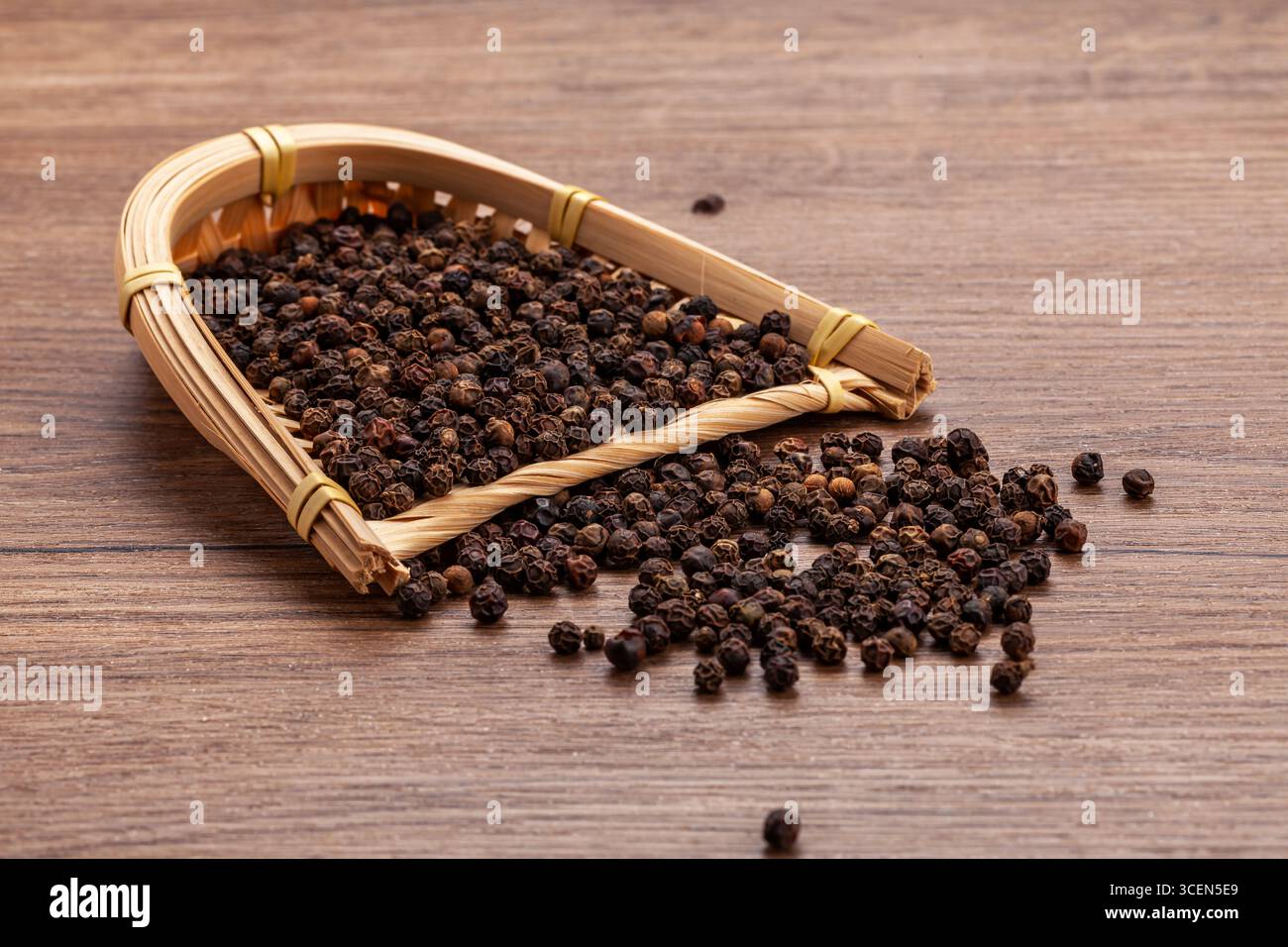 Grains de poivre noir dans le panier de bambou sur la table en bois - fond culinaire Banque D'Images