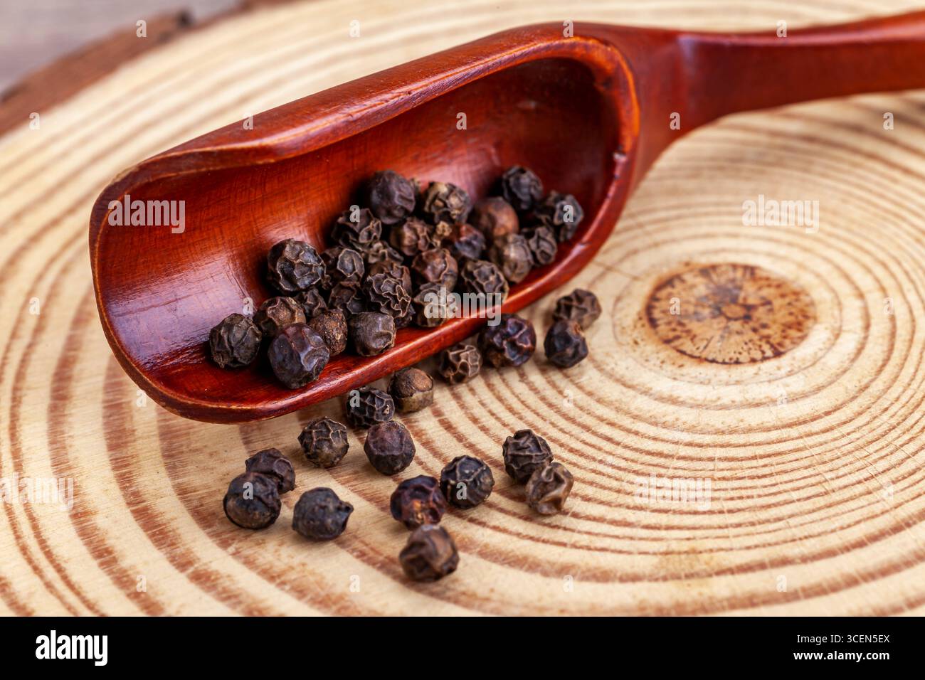 Gros plan de grains de poivre noir dans une pelle en bois sur une planche à découper ronde rustique en bois Banque D'Images