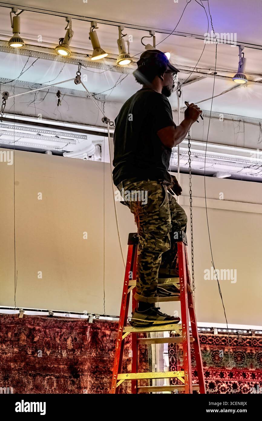 New York, USA - 13 juin 2025 : électricien sur une échelle réparant des plafonniers à l'intérieur. travail, énergie, personne, moderne, Banque D'Images