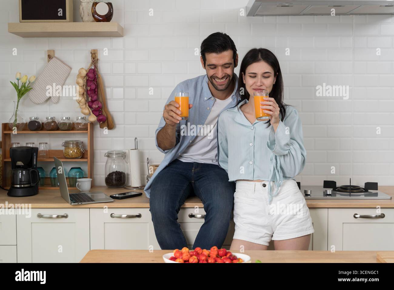 Jeune couple appréciant le jus d'orange frais dans la cuisine moderne, style de vie décontracté, amour et relation, matin joyeux ensemble, boisson saine, positiv Banque D'Images
