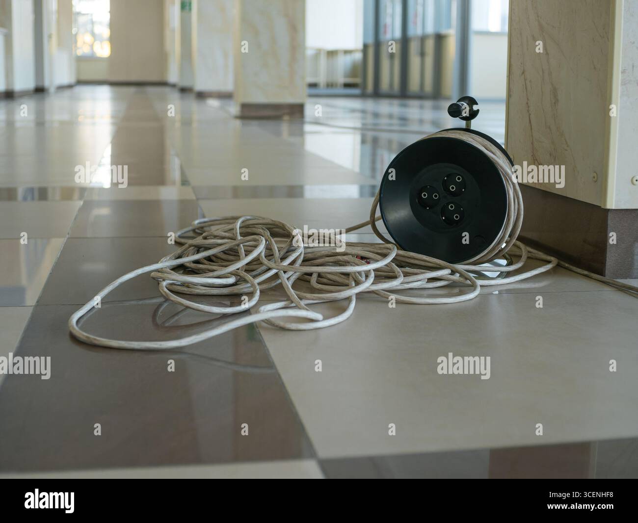 Une bobine avec une rallonge déroulée sur le sol dans un hall moderne spacieux. Banque D'Images