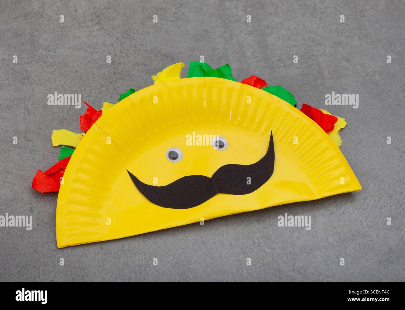 une assiette en papier jaune pliée pour faire un taco artisanal. le taco a des yeux et une moustache. le papier coloré représente le remplissage Banque D'Images