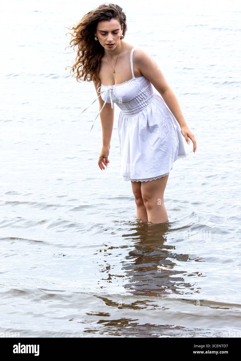 Tayport à Fife, en Écosse. Femme à la mode portant une robe blanche courte se tient dans la rivière Tay lors d'une séance photo sur le thème de la fantaisie l'après-midi, Royaume-Uni Banque D'Images