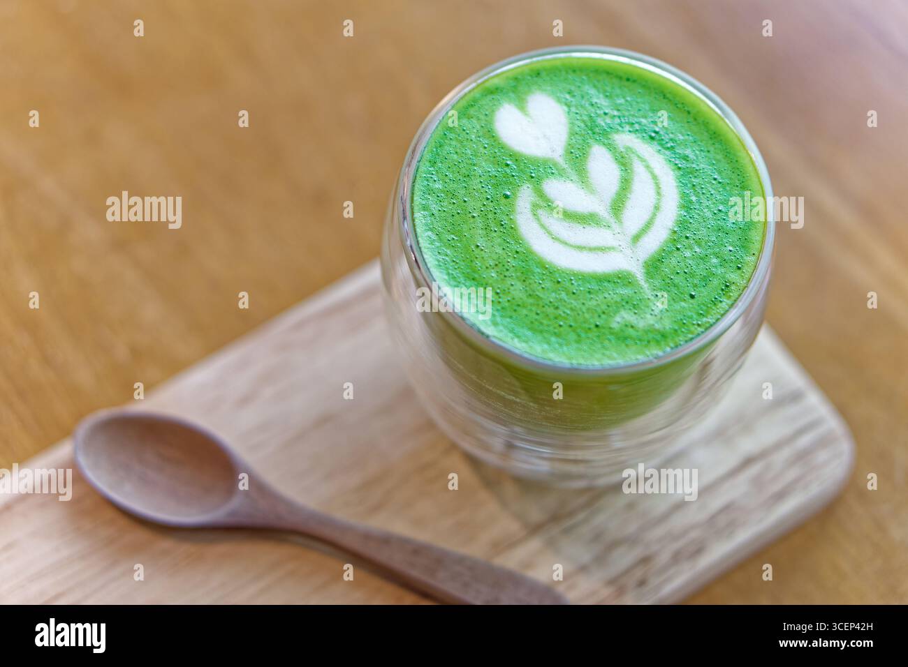 Latte Matcha avec art en forme de coeur en verre sur plateau en bois. Latte matcha chaud avec cœur délicat et feuilles servi dans une tasse en verre à double paroi Banque D'Images