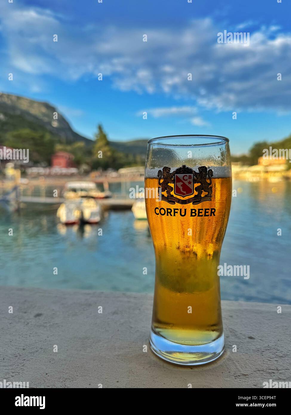 Un verre de bière de Corfou avec la plage de Paleokastritsa derrière, Corfou, Grèce. - Image de stock capturée avec un smartphone