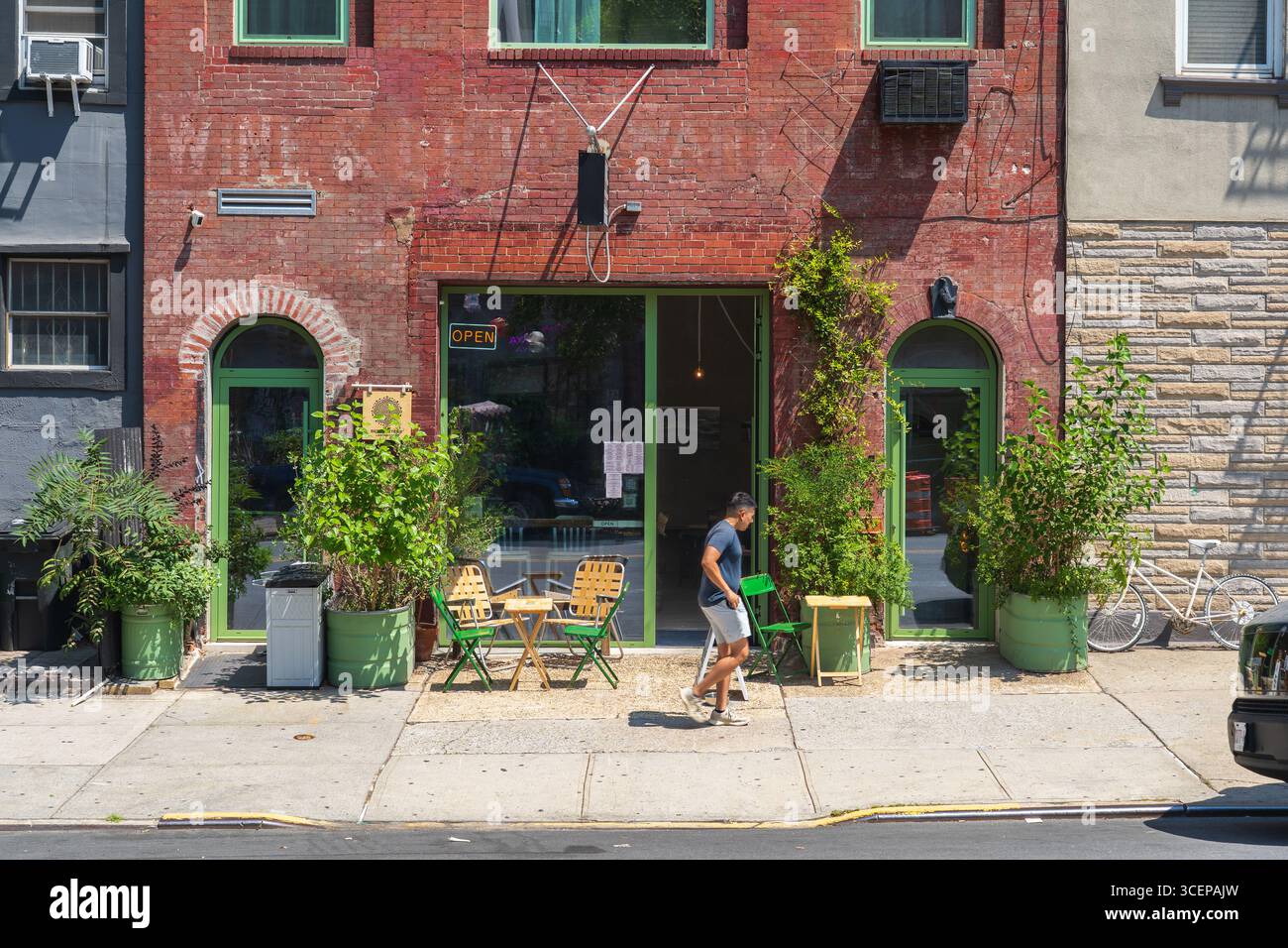 Brooklyn, États-Unis - 10 août 2025 : vue d'une façade de bâtiment en briques rouges avec des accents verts vibrants, des plantes et un homme marchant, créant une scène urbaine animée. Banque D'Images