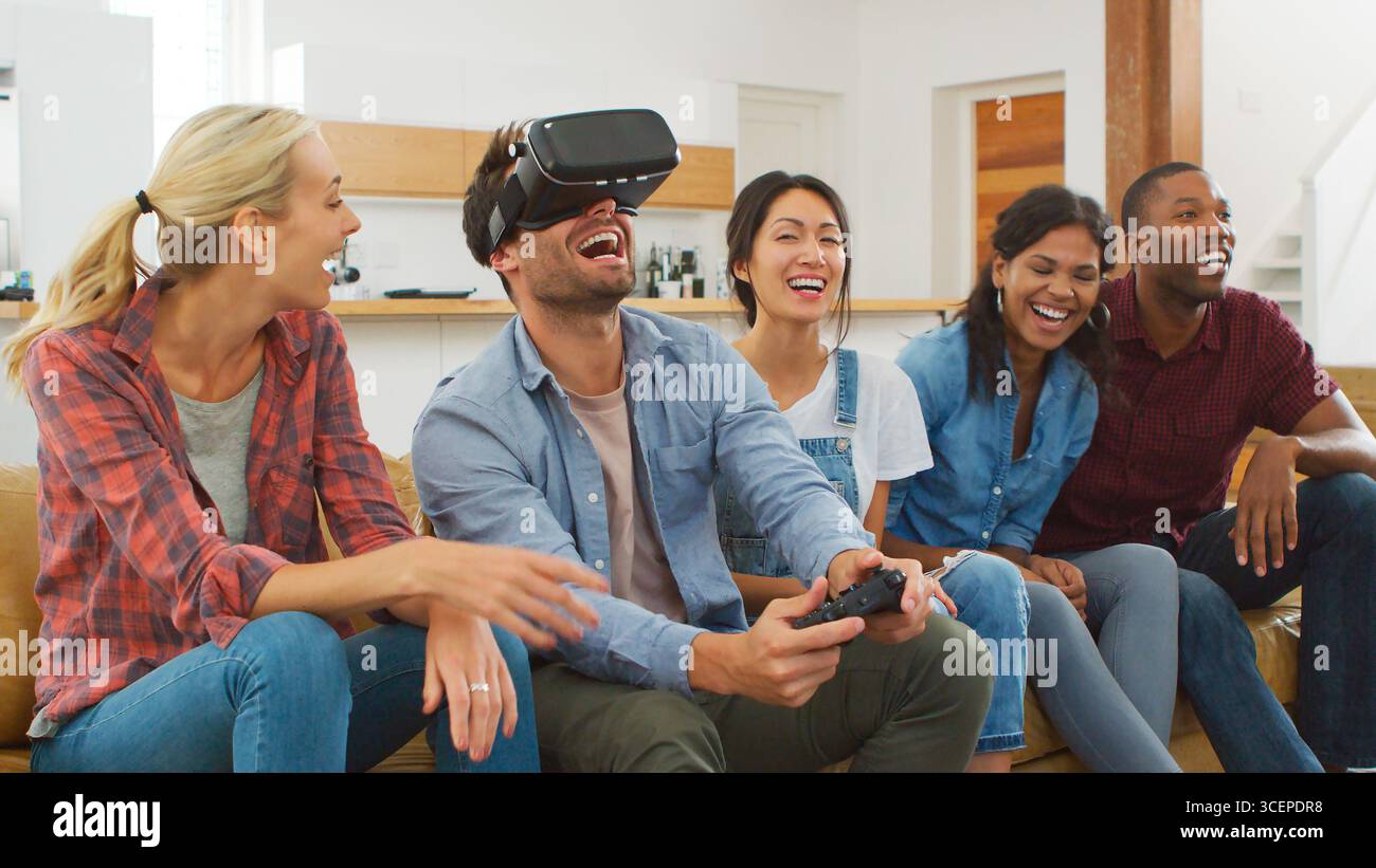 Groupe d'amis multiculturels jouant à un jeu informatique avec casque de réalité virtuelle à la maison Banque D'Images