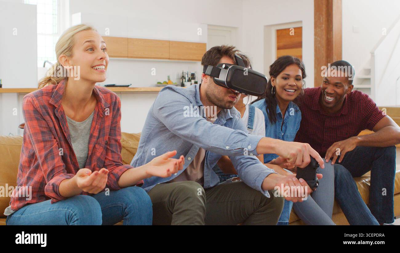 Groupe d'amis multiculturels jouant à un jeu informatique avec casque de réalité virtuelle à la maison Banque D'Images