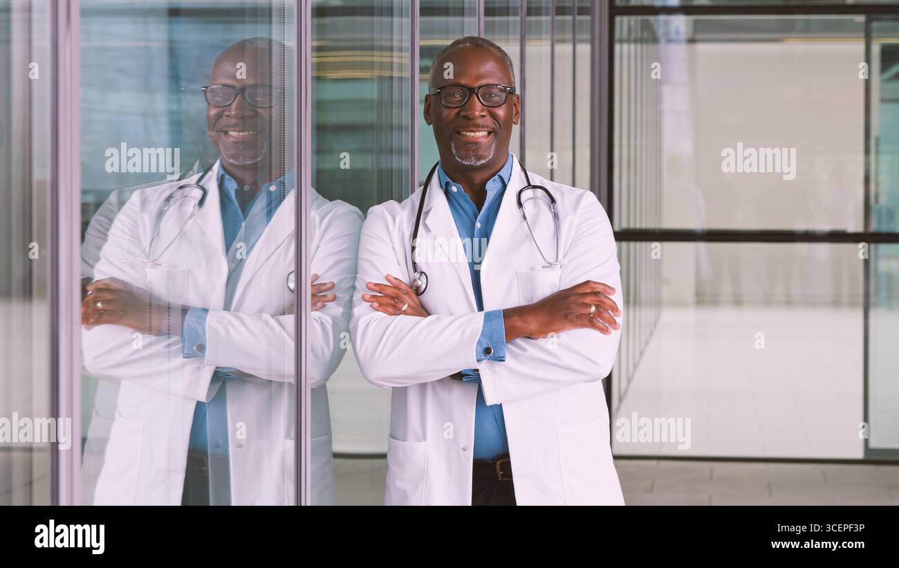 Portrait d'un médecin masculin senior souriant portant un manteau blanc debout dans le bâtiment de l'hôpital moderne Banque D'Images