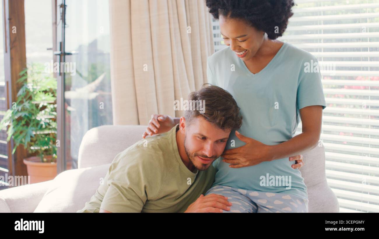 Couple multi-racial avec femme enceinte dans la chambre à coucher à la maison avec l'homme écoutant le battement de coeur de bébé Banque D'Images