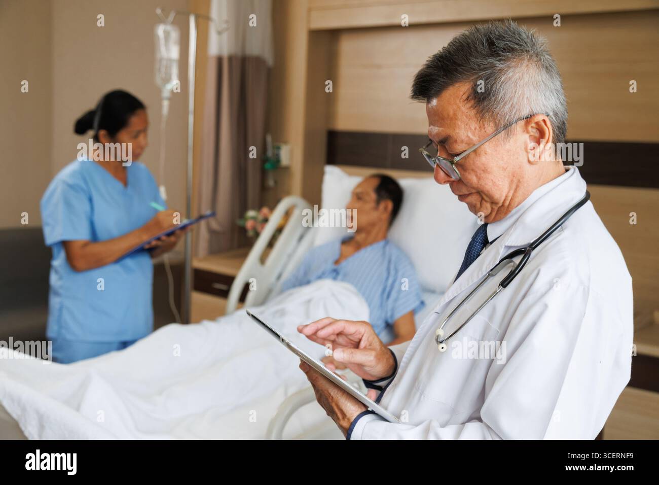 médecin professionnel masculin senior asiatique utilisant la tablette pour le dossier de santé numérique et l'infirmière écrit des notes à côté du patient. chambre d'hôpital équipée médicale in Banque D'Images médecin professionnel masculin senior asiatique utilisant la tablette pour le dossier de santé numérique et l'infirmière écrit des notes à côté du patient. chambre d'hôpital équipée médicale in Banque D'Images