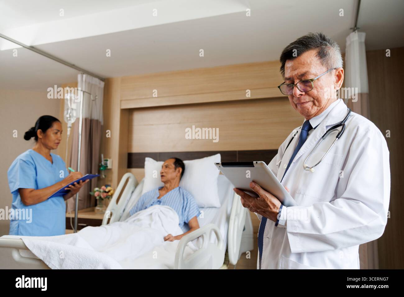 médecin professionnel masculin senior asiatique utilisant la tablette pour le dossier de santé numérique et l'infirmière écrit des notes à côté du patient. chambre d'hôpital équipée médicale in Banque D'Images médecin professionnel masculin senior asiatique utilisant la tablette pour le dossier de santé numérique et l'infirmière écrit des notes à côté du patient. chambre d'hôpital équipée médicale in Banque D'Images