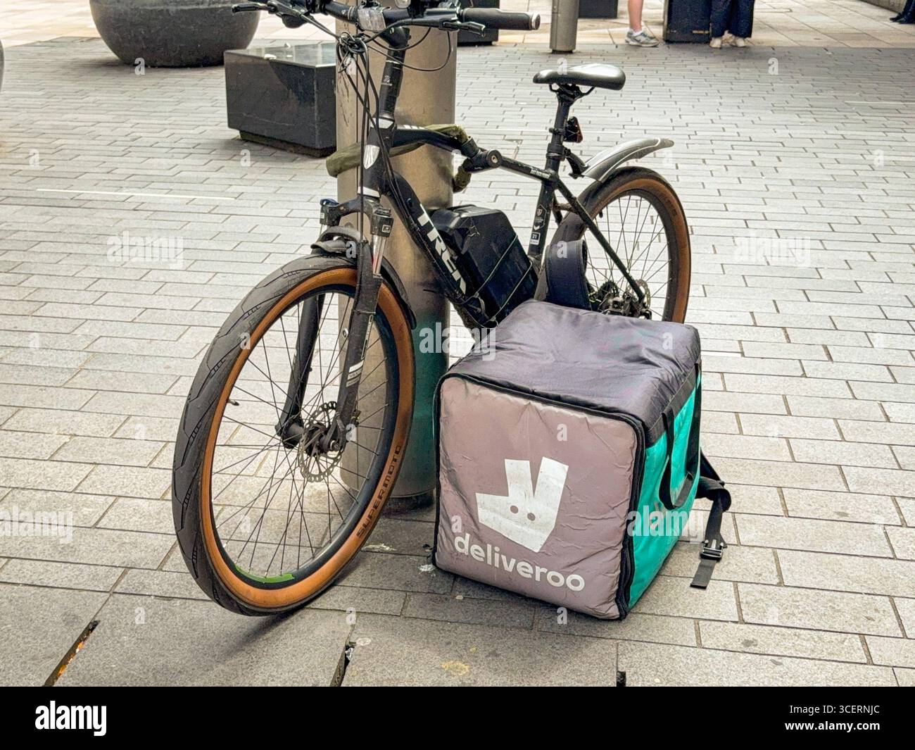 Cardiff, pays de Galles, Royaume-Uni - 16 juillet 2025 : conteneur isotherme pour le service de livraison de plats à emporter de Deliveroo, accompagné du vélo électrique d'un livreur Banque D'Images