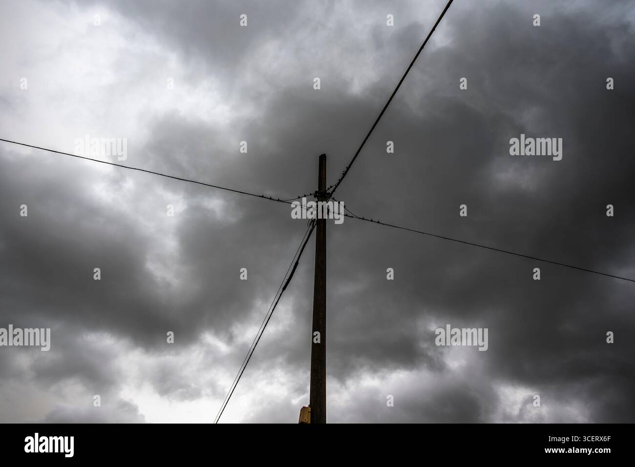 Silhouette d'un poteau utilitaire avec des câbles qui se croisent formant un motif croisé contre un ciel sombre et nuageux. Une image dramatique symbolisant la tension, conne Banque D'Images