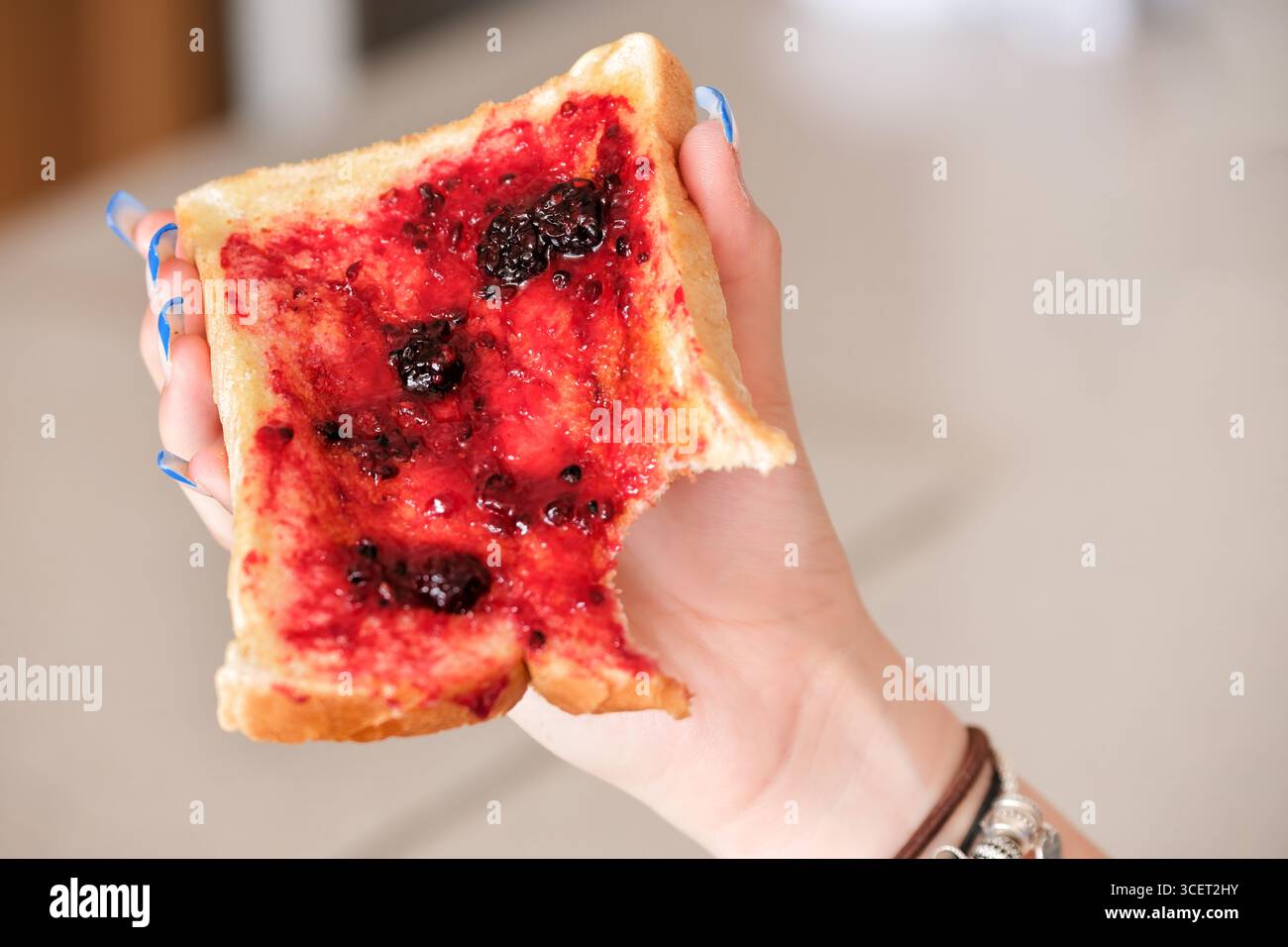ROYAUME-UNI. Une personne dans leur maison tenant une tranche de pain grillé fraîchement préparé tartiné avec du beurre et de la confiture de mûres. Banque D'Images