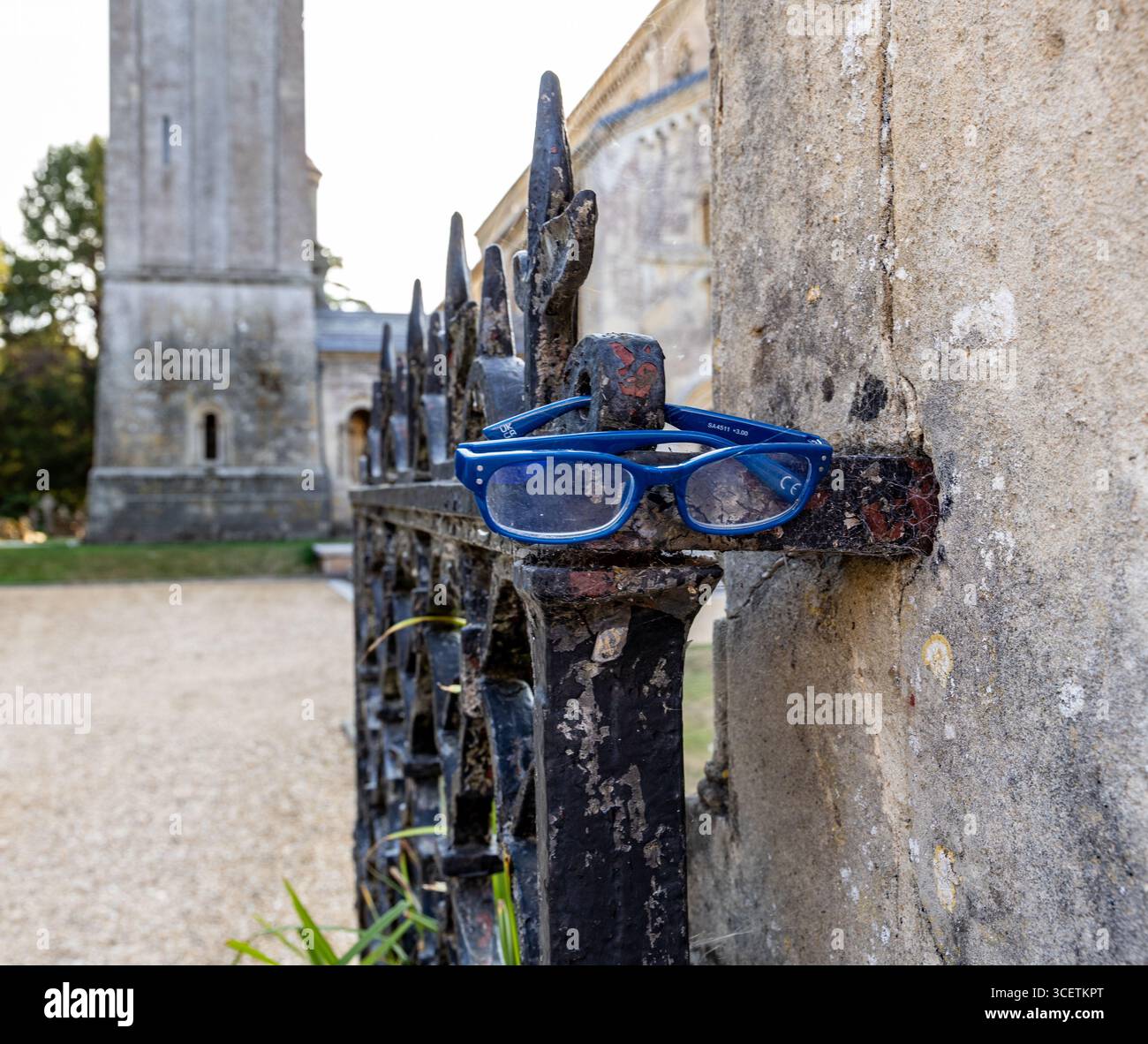 Une paire de lunettes bleues reposant sur une porte de fer rustique avec un bâtiment historique de l'église en pierre en arrière-plan. Wilton Salisbury Royaume-Uni Banque D'Images