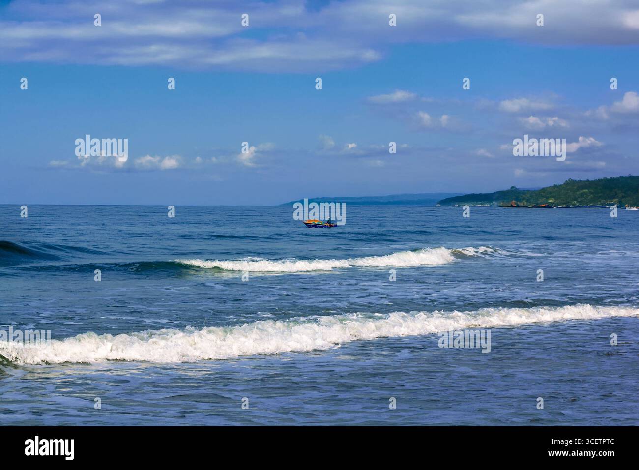 Vue panoramique sur un bord de mer calme avec de douces vagues océaniques, un bateau de pêche à l'horizon sous un ciel dégagé. Golden Hour shot Banque D'Images