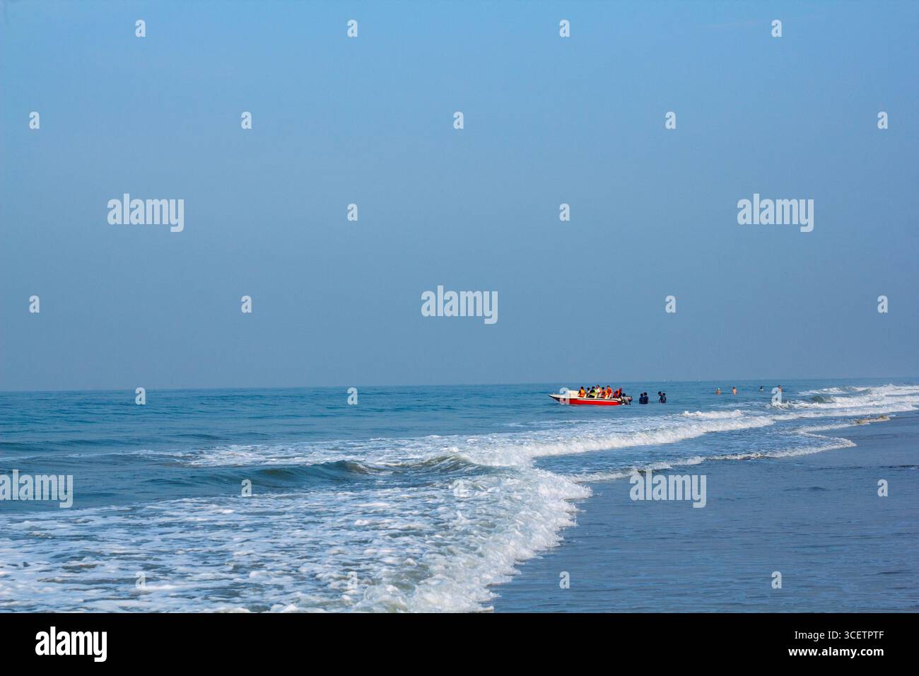 Vue panoramique sur un bord de mer calme avec de douces vagues océaniques, un bateau de pêche à l'horizon sous un ciel dégagé. Golden Hour shot Banque D'Images