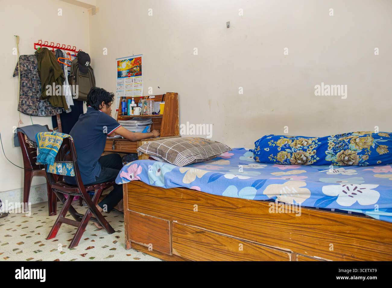 Apprenant concentré au bureau organisé à côté du lit avec draps floraux dans une auberge étudiante Banque D'Images