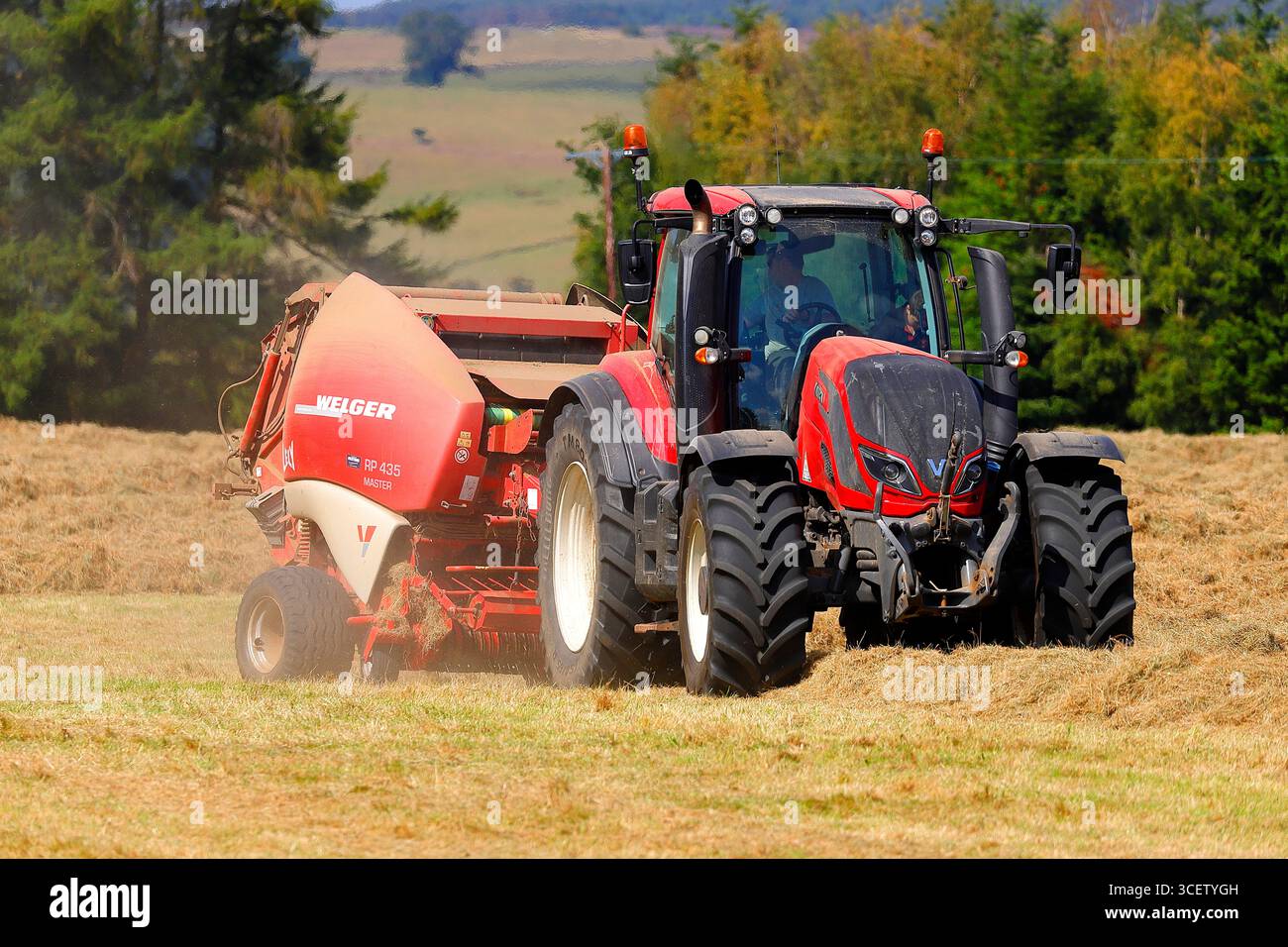 Tracteur rouge fabriquant des balles de foin avec une presse Welger dans un champ sur le Swinton Estate dans le North Yorkshire, au Royaume-Uni Banque D'Images