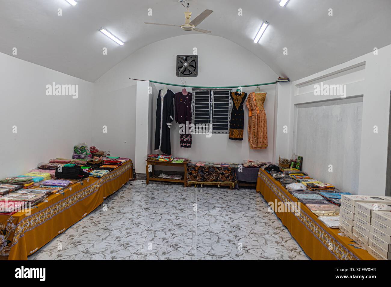 Intérieur de magasin de vêtements traditionnels bien éclairé avec des vêtements colorés soigneusement disposés sur les tables et les murs Banque D'Images