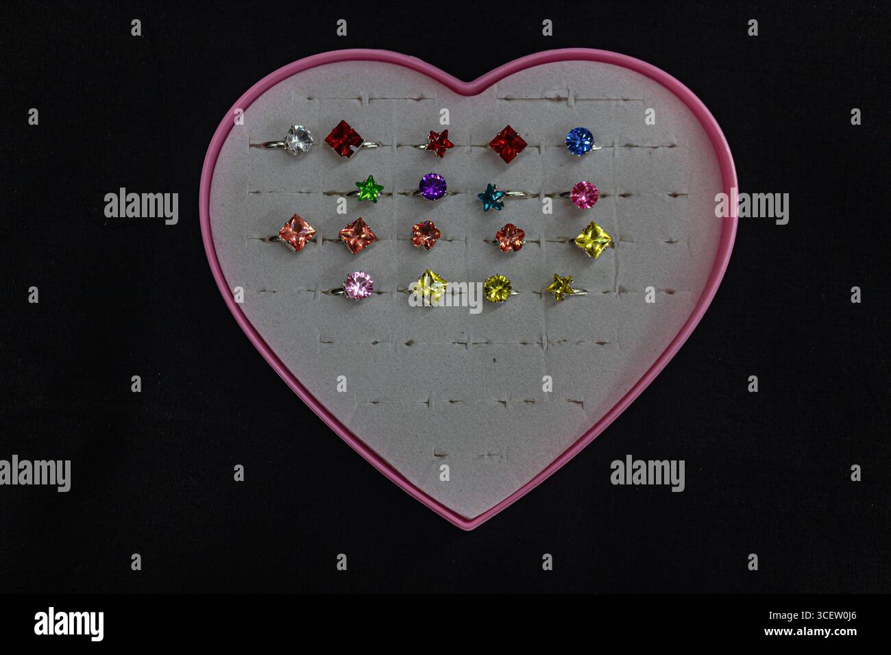 Anneaux mignons pour enfants avec des dessins de bande dessinée disposés dans une boîte en forme de coeur sur fond noir Banque D'Images