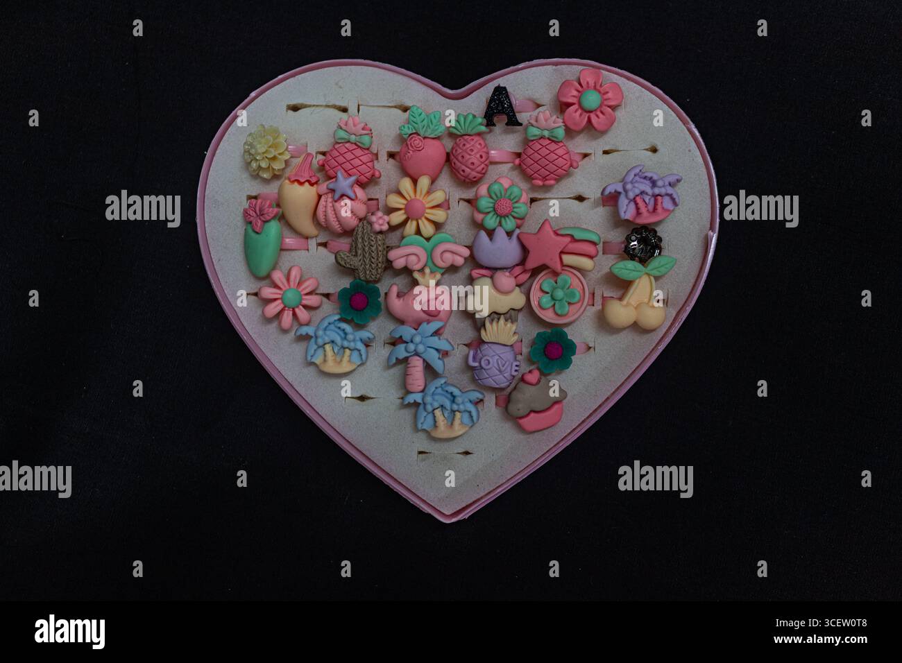 Fruits ludiques et anneaux en forme de fleur organisés attrayamment dans un porte-bijoux rose en forme de coeur Banque D'Images