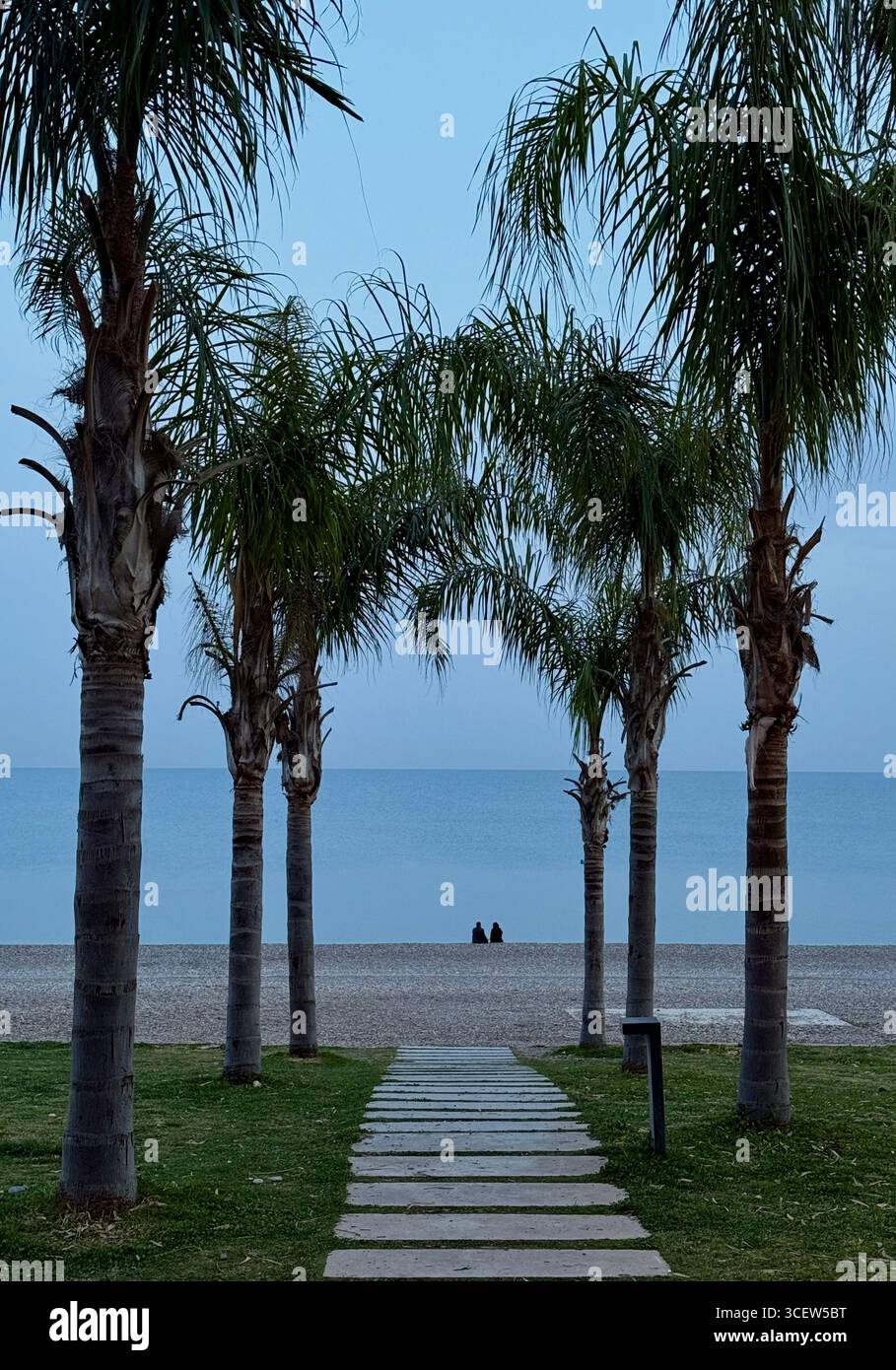 Turkiye, Antalya, Konyallti 03/31/2025.soir le temps de la mer. Deux personnes assises sur le rivage. Ambiance romantique. Paumes hautes - Image de stock capturée avec un smartphone