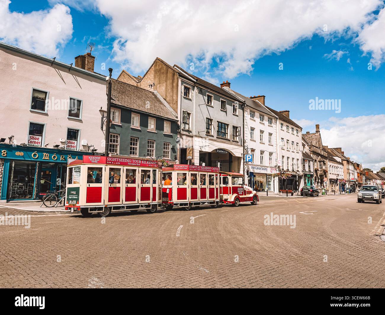 Un train rouge et blanc descend une rue devant un bâtiment avec un panneau qui dit "Orchard." Kilkenny, Irlande Banque D'Images