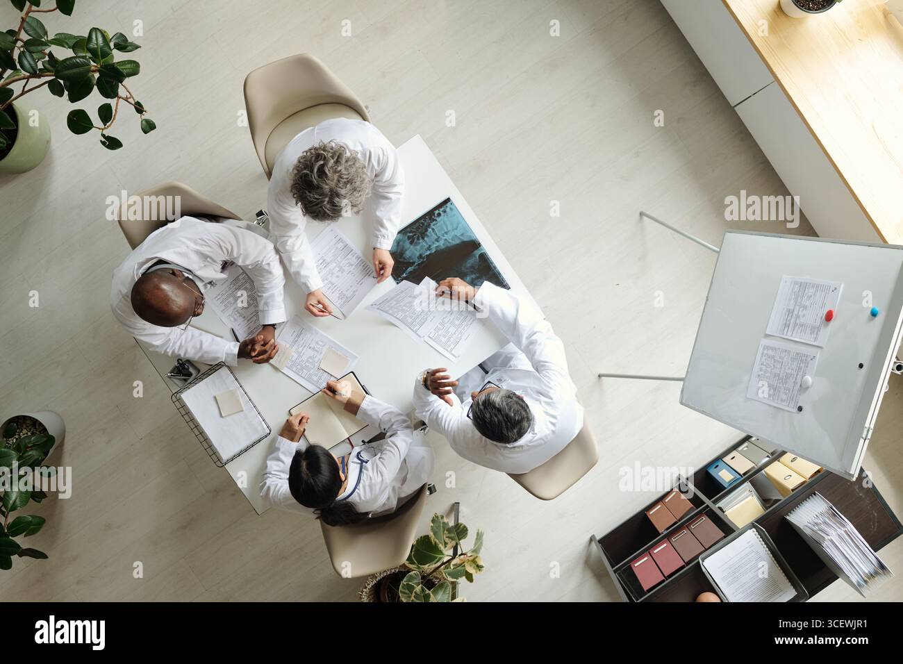 Groupe de médecins multiethniques d'âge moyen discutant des documents médicaux autour de la table, collaborant sur les soins aux patients, examinant des graphiques et prenant des notes, vue de dessus des professionnels de la santé Banque D'Images