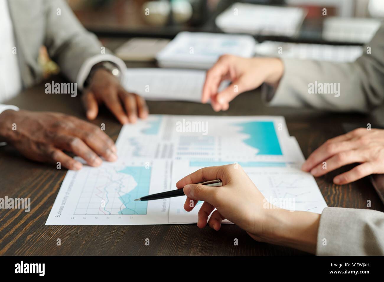 Vue de dessus montrant les mains d'une femme caucasienne d'âge moyen, d'un homme noir d'âge moyen et d'un homme caucasien d'âge moyen analysant les graphiques financiers et discutant de la stratégie commerciale au bureau Banque D'Images