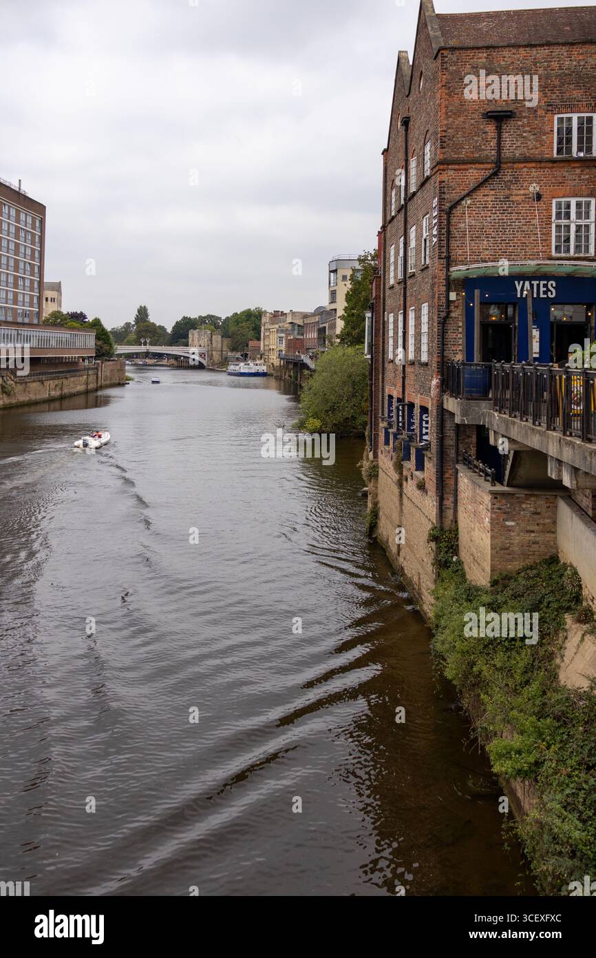 Rivière de la ville bordée de bâtiments et d'appartements en briques, avec des cygnes nageant sur l'eau sous un ciel nuageux Banque D'Images