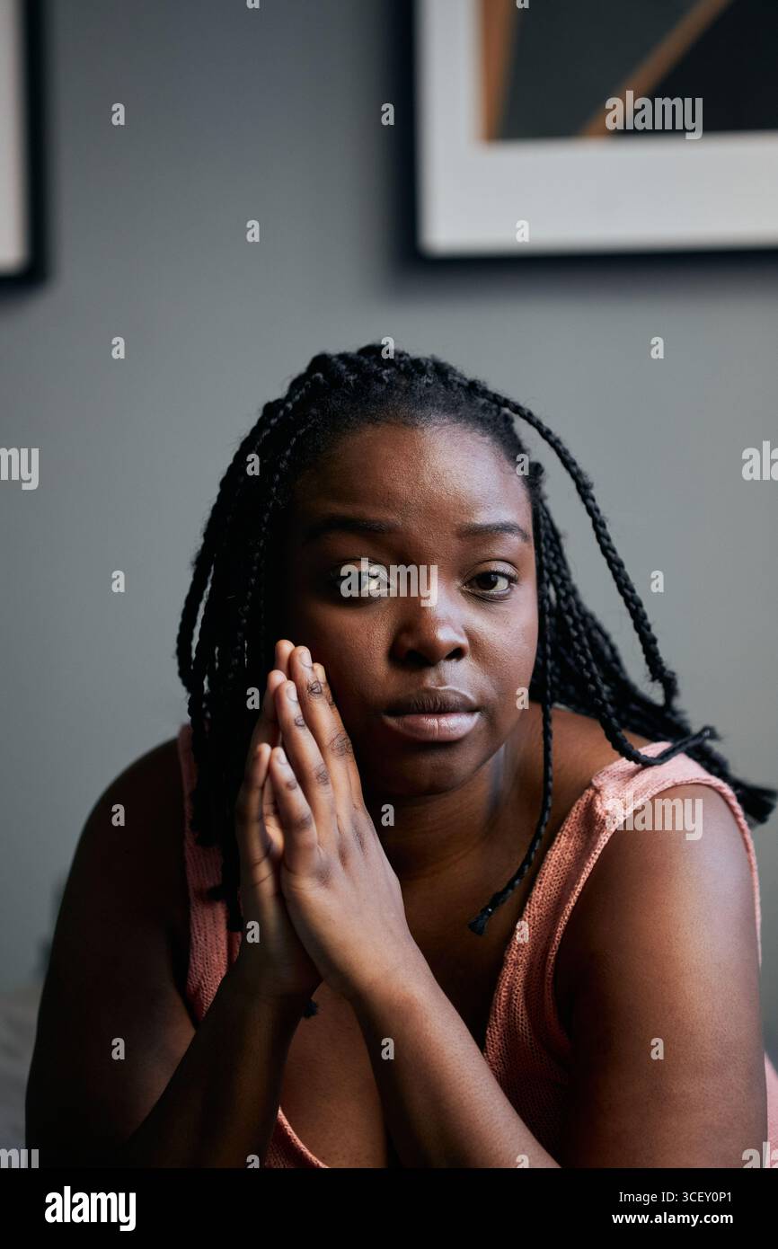 Gros plan vertical moyen de la belle jeune femme noire assise dans la chambre à coucher à la maison regardant la caméra Banque D'Images