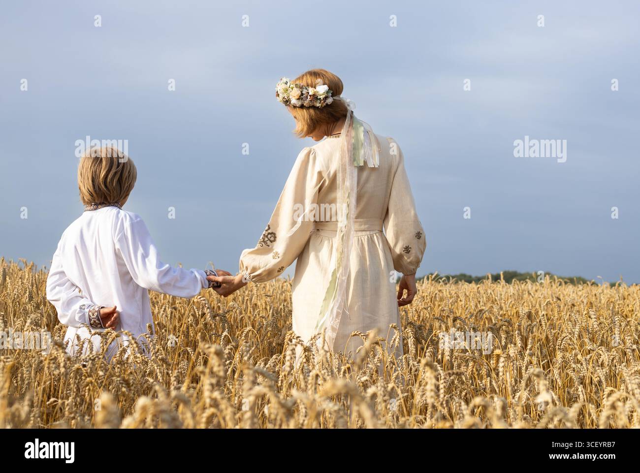 femme dans une robe brodée tient la main d'un enfant debout avec son dos entre les oreilles de blé dans un champ par une journée ensoleillée. Famille ukrainienne, unité, supp Banque D'Images